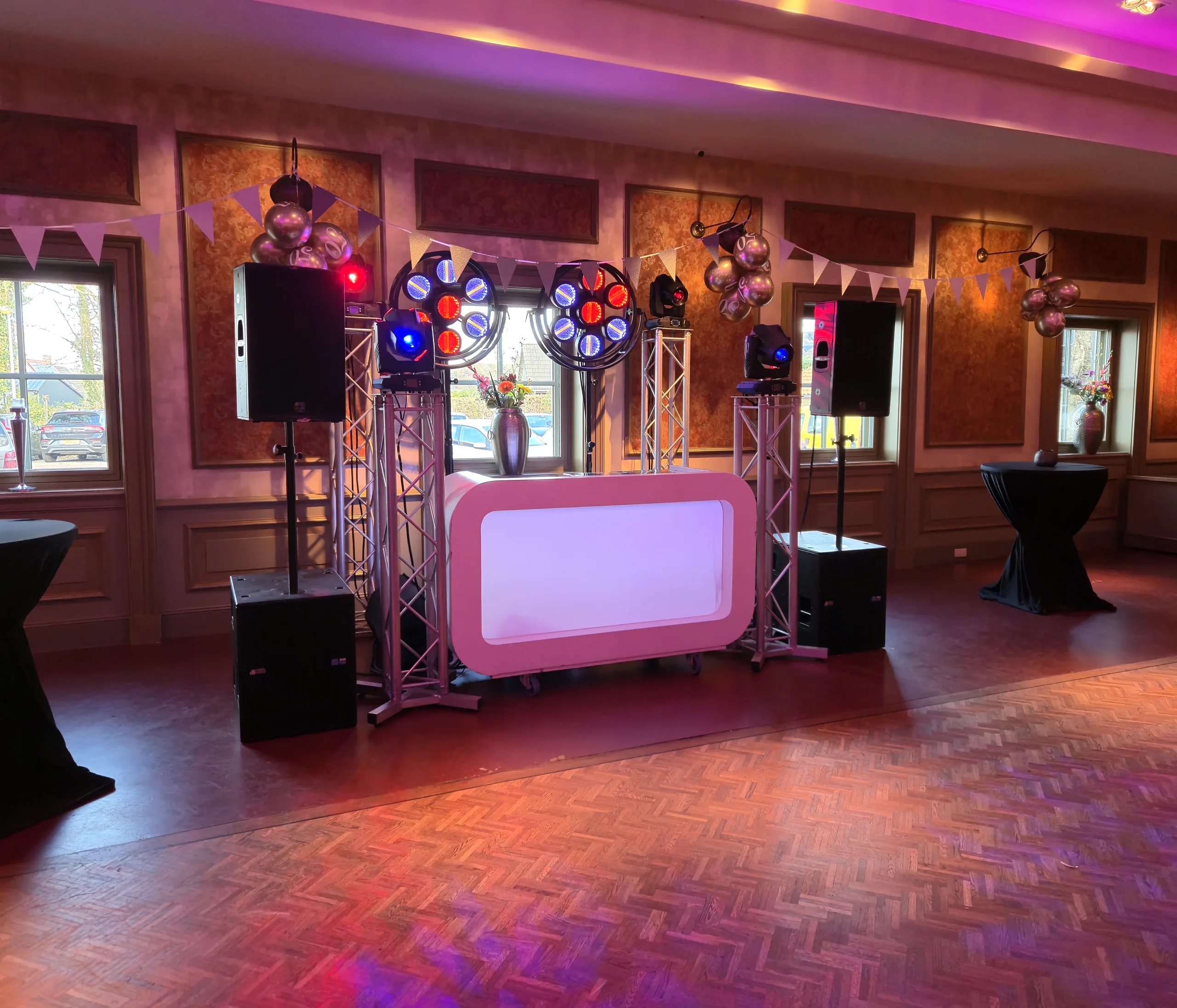 Verlichte DJ-booth met truss en roze uplights in De Postwagen in Tolbert