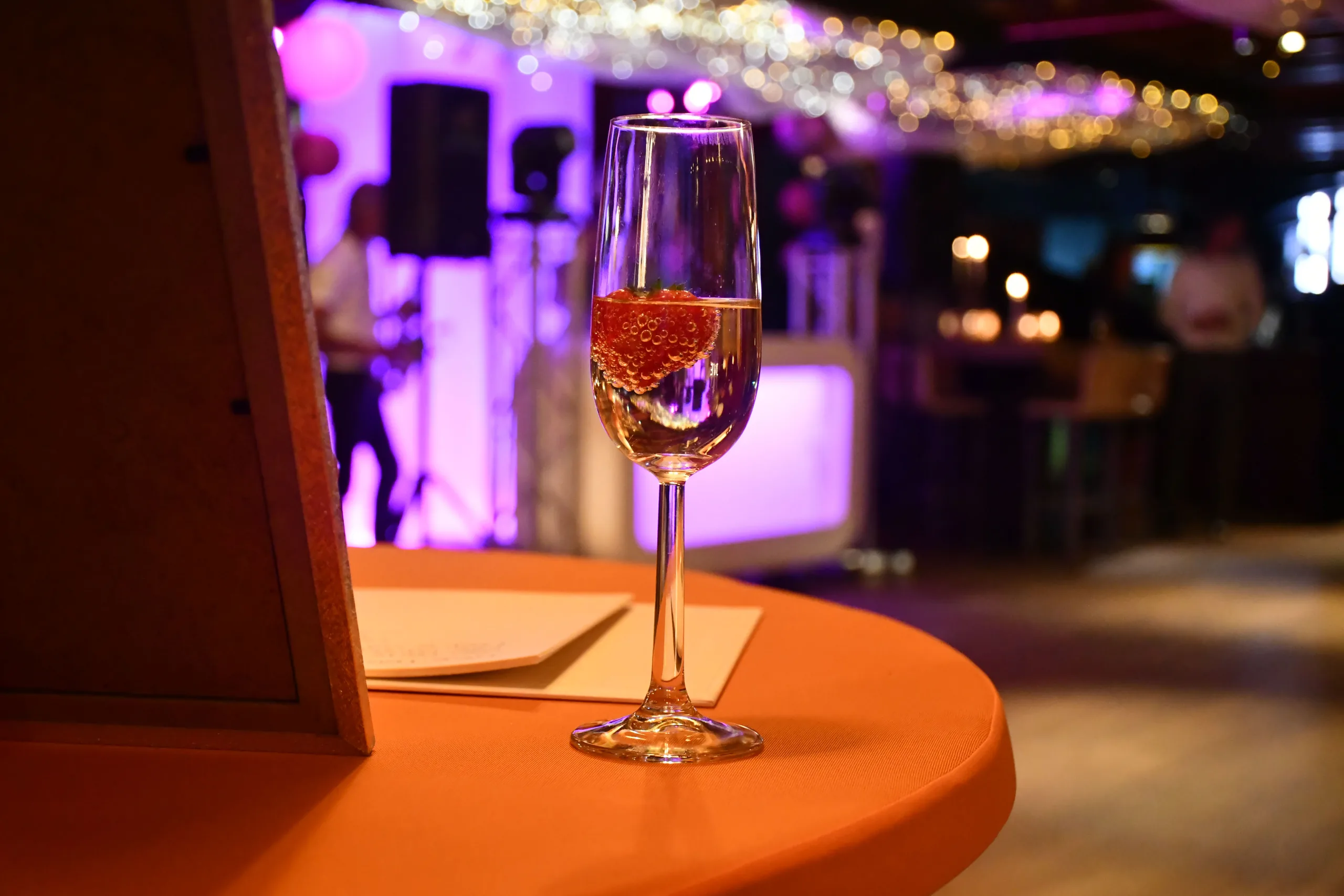 Champagneglas op een statafel met de verlichte DJ-booth onscherp op de achtergrond