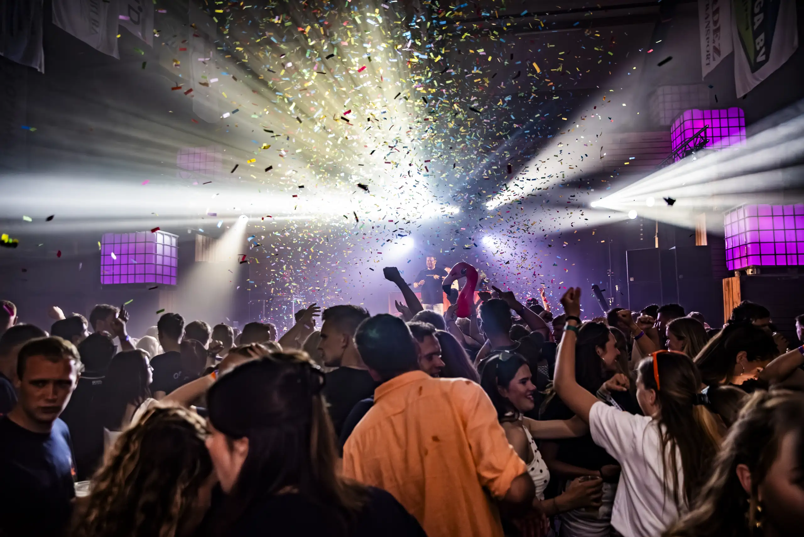 Confetti boven de volle dansvloer met lichtbundels tijdens een schuurfeest