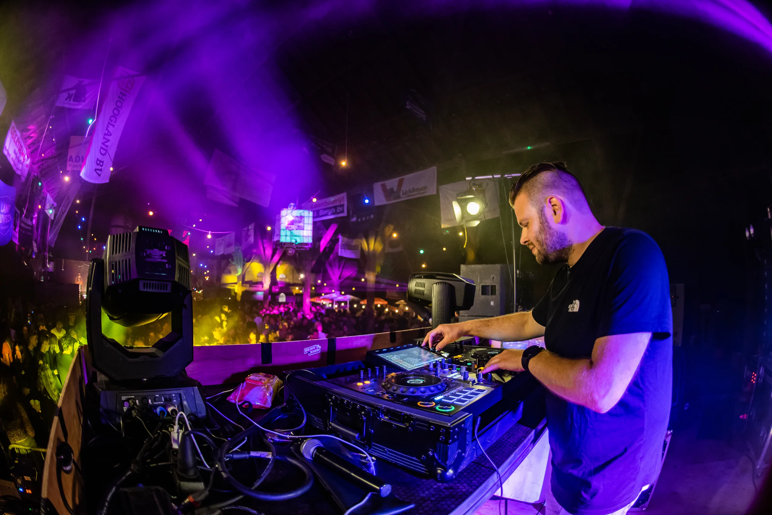 DJ Martijn Renkema achter de booth met paarse moving heads en rook tijdens een schuurfeest