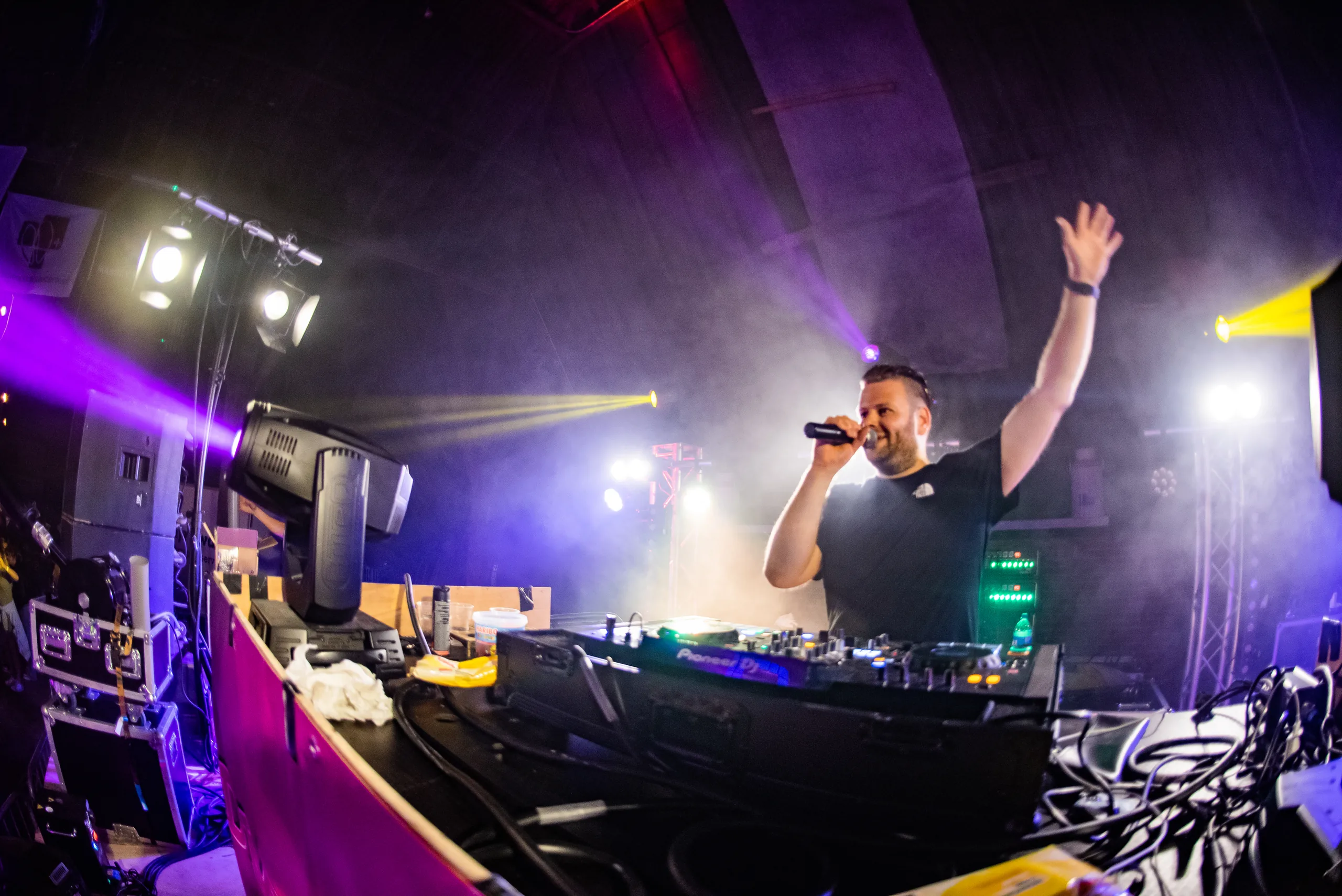 DJ Martijn Renkema met microfoon en de arm omhoog achter de booth tijdens een schuurfeest