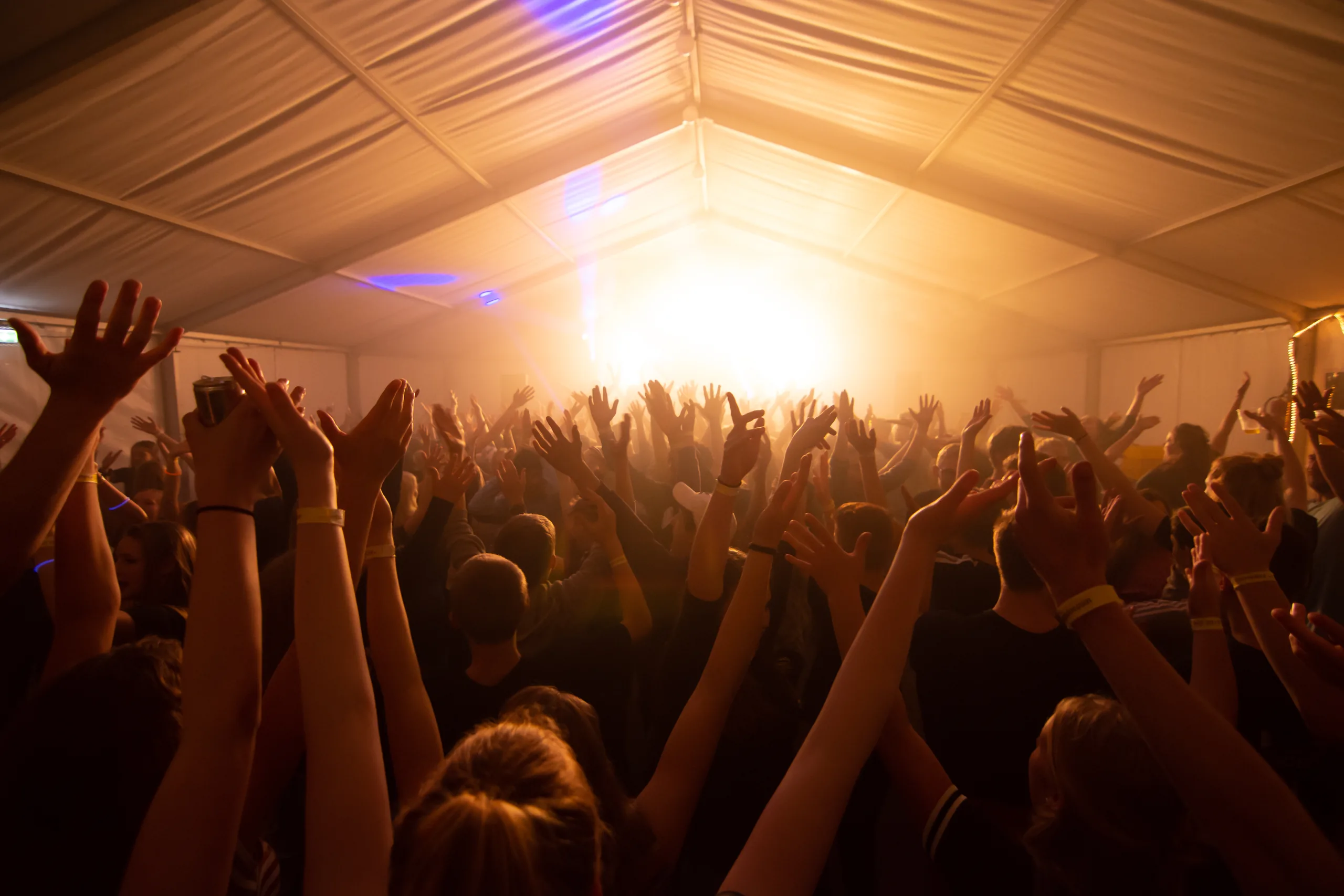 Publiek met de handen in de lucht in de feesttent tijdens het MJT-volleybaltoernooi