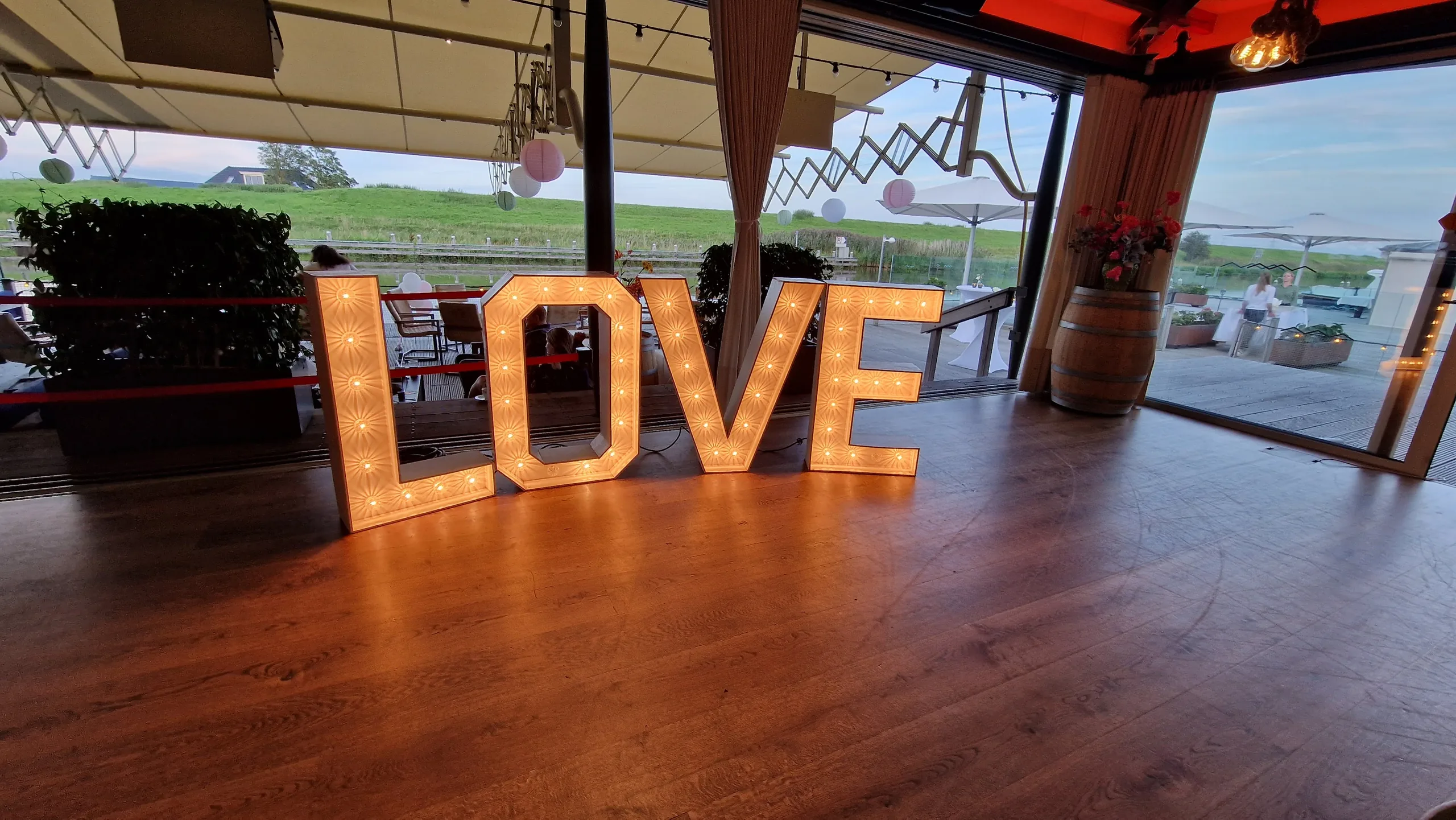 Verlichte LOVE-letters op de dansvloer van een feestzaal met uitzicht over het weiland