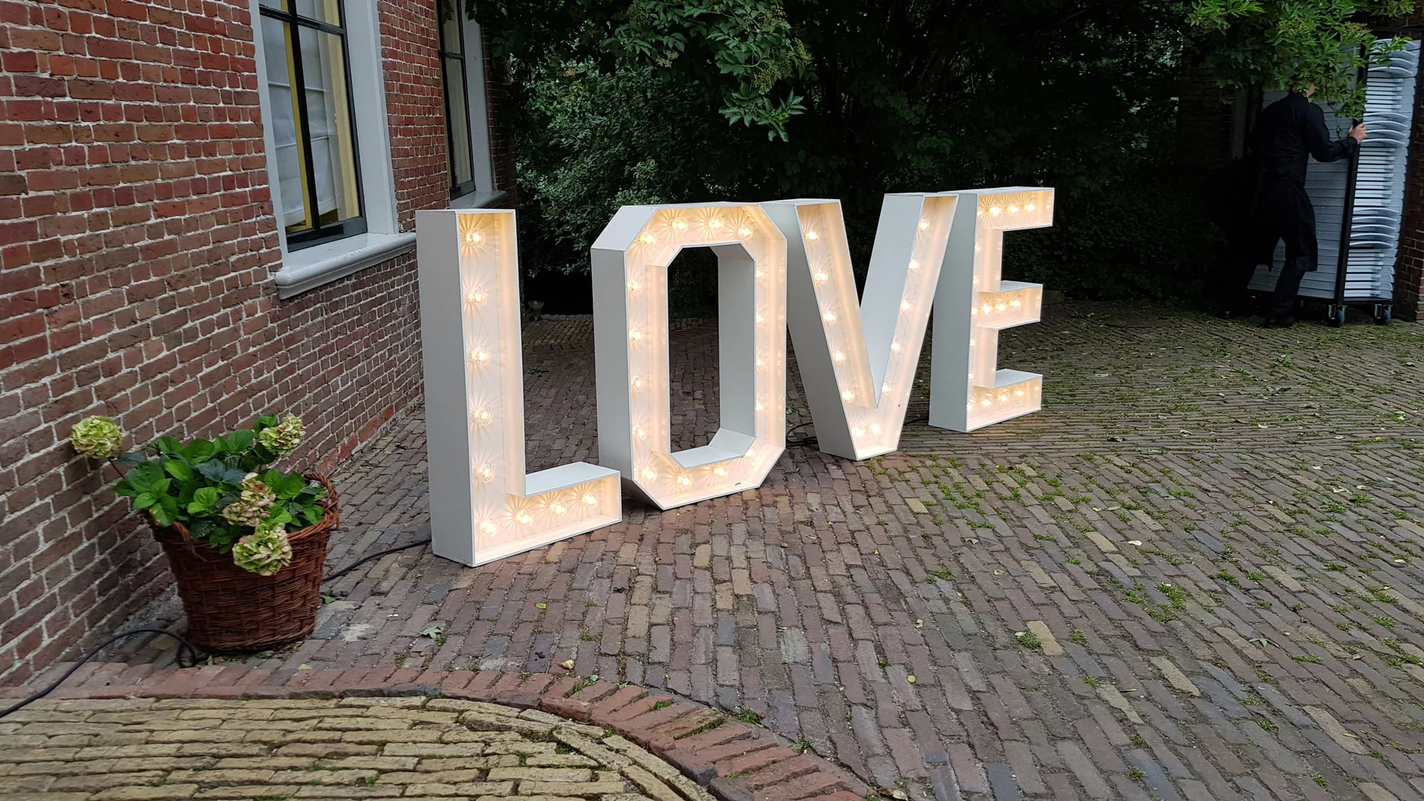 Verlichte LOVE-letters tegen de bakstenen muur van een trouwlocatie