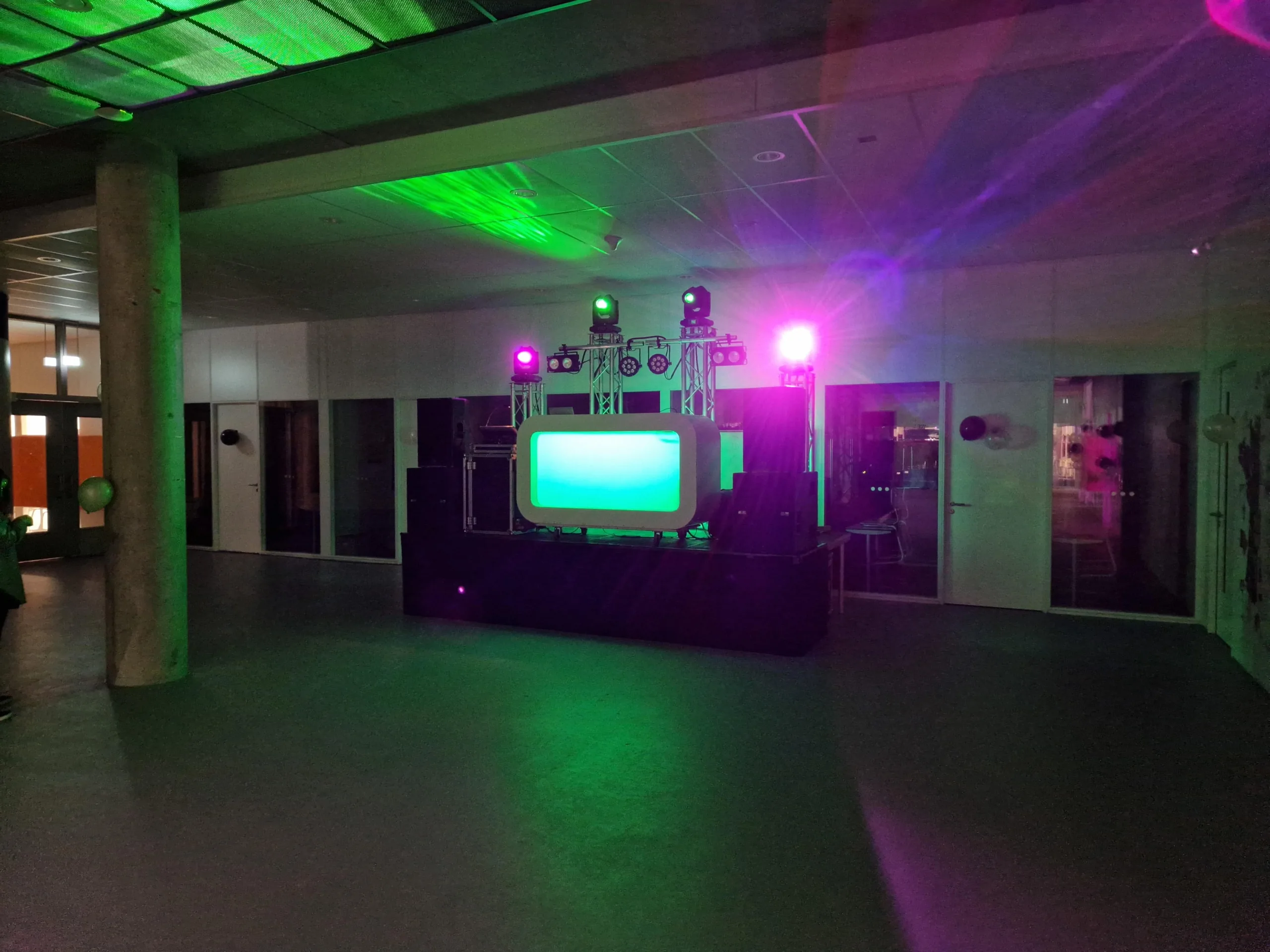 Schoolhal met DJ-booth onder groene en paarse belichting tijdens een schoolfeest