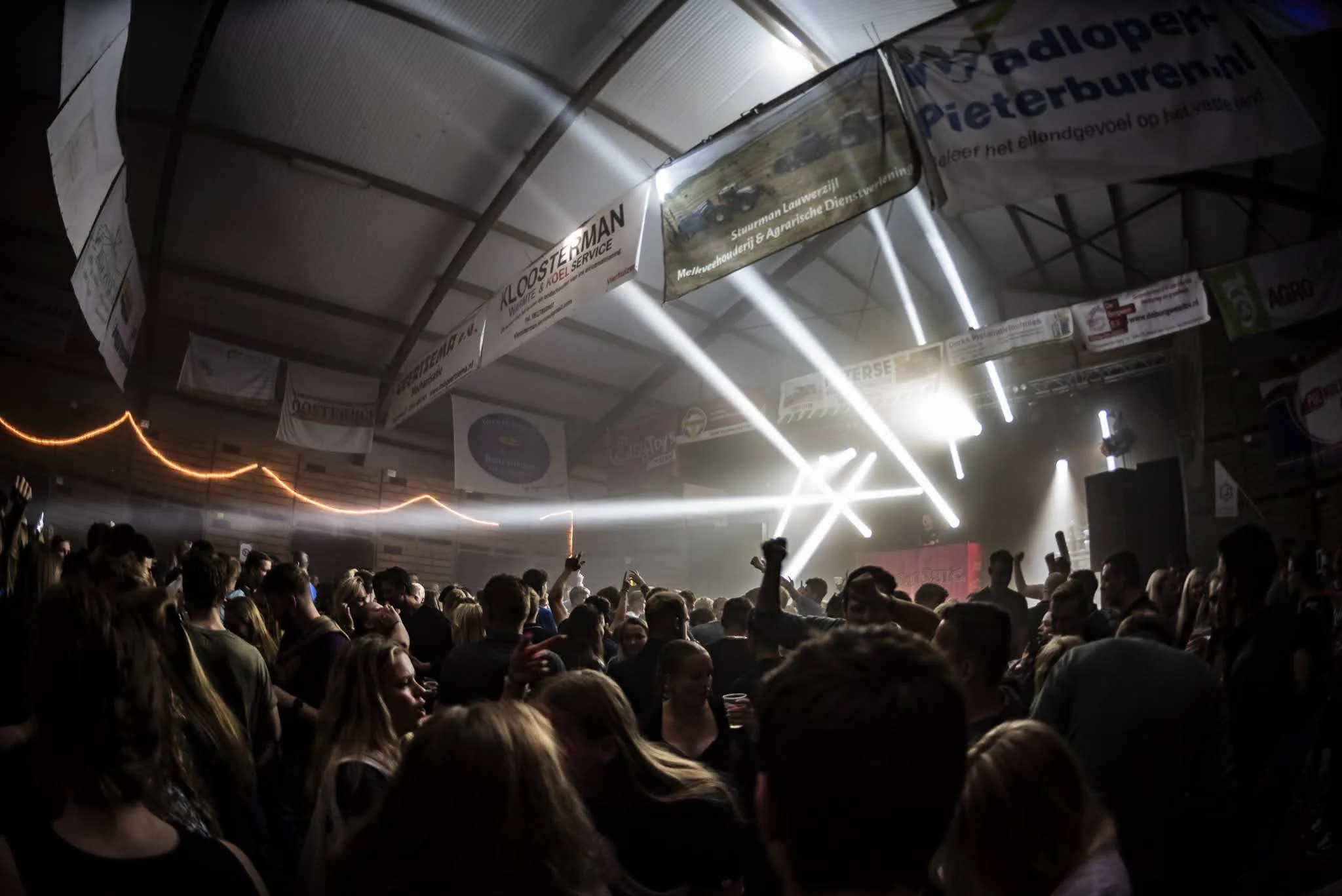Volle schuur met publiek en witte lichtbundels tussen de spanten