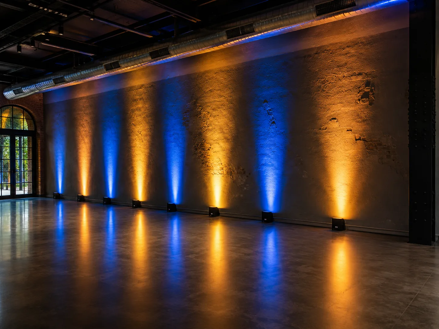 Uplights in afwisselend blauw en oranje tegen een bakstenen wand